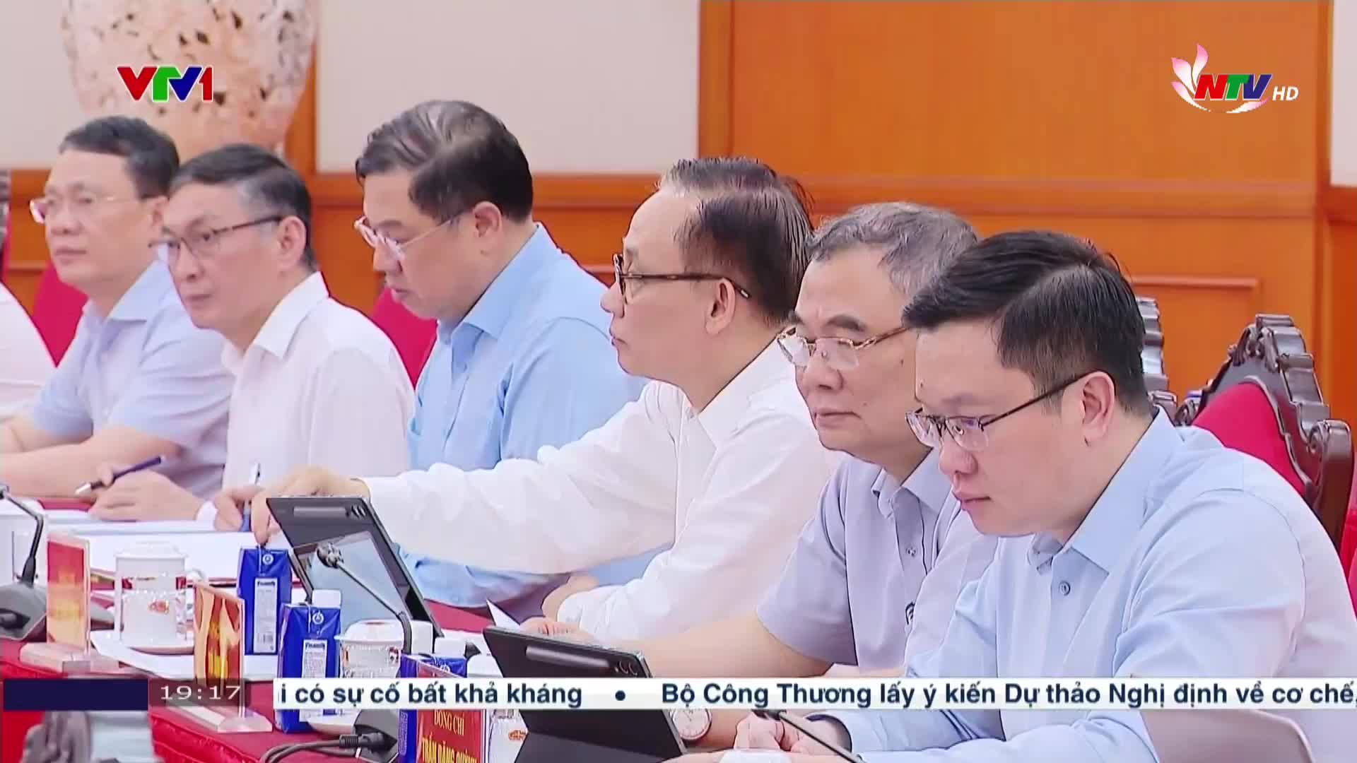 A group of men in shirts sit around a long table, mostly facing forward. The broadcast from Nghe An TV in Vietnam displays text at the bottom of the screen.
