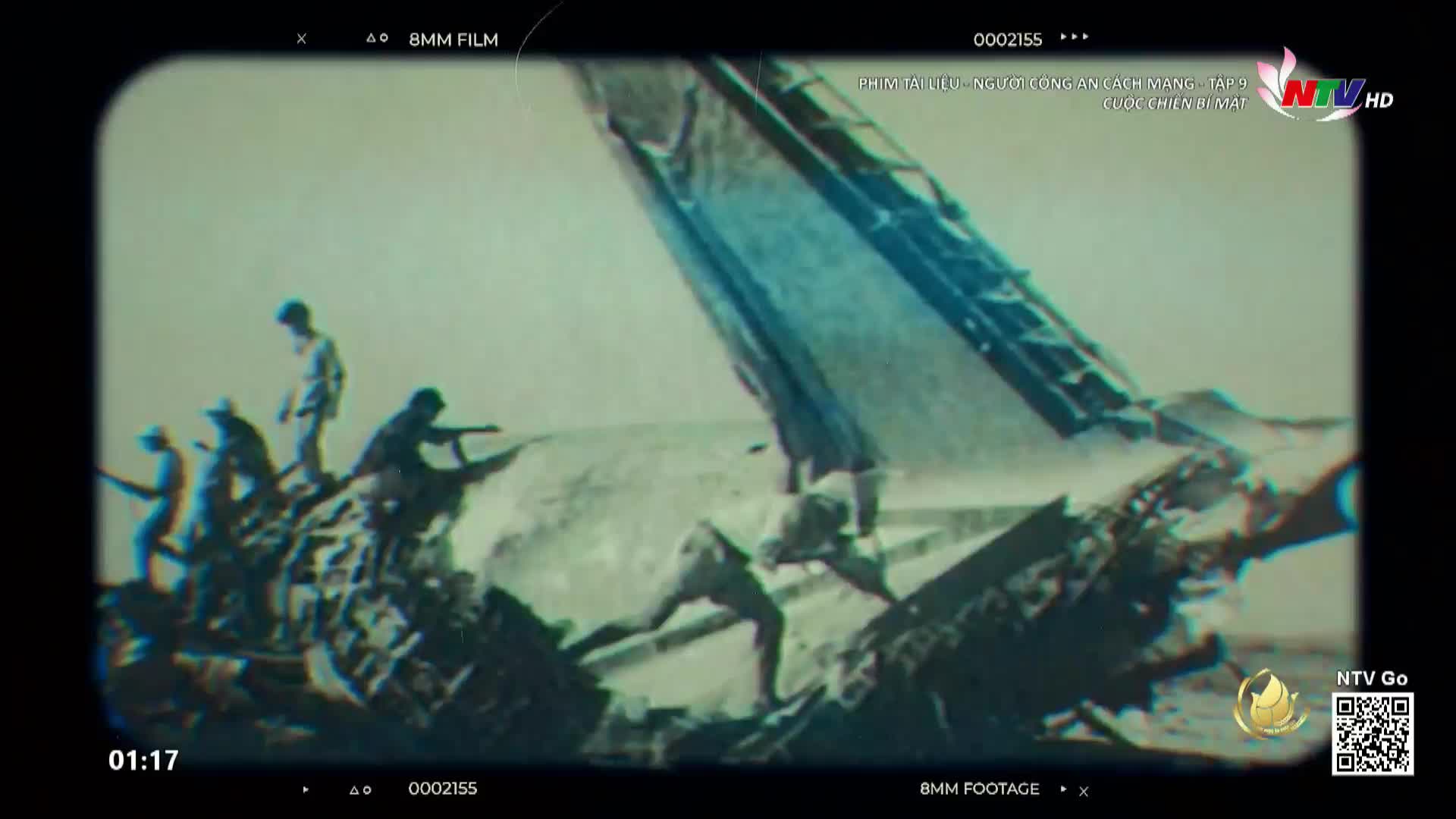 Men scramble across the wreckage of what looks like a downed aircraft, some aiming rifles. The scene is from what Nghe An TV is calling 8mm footage.
