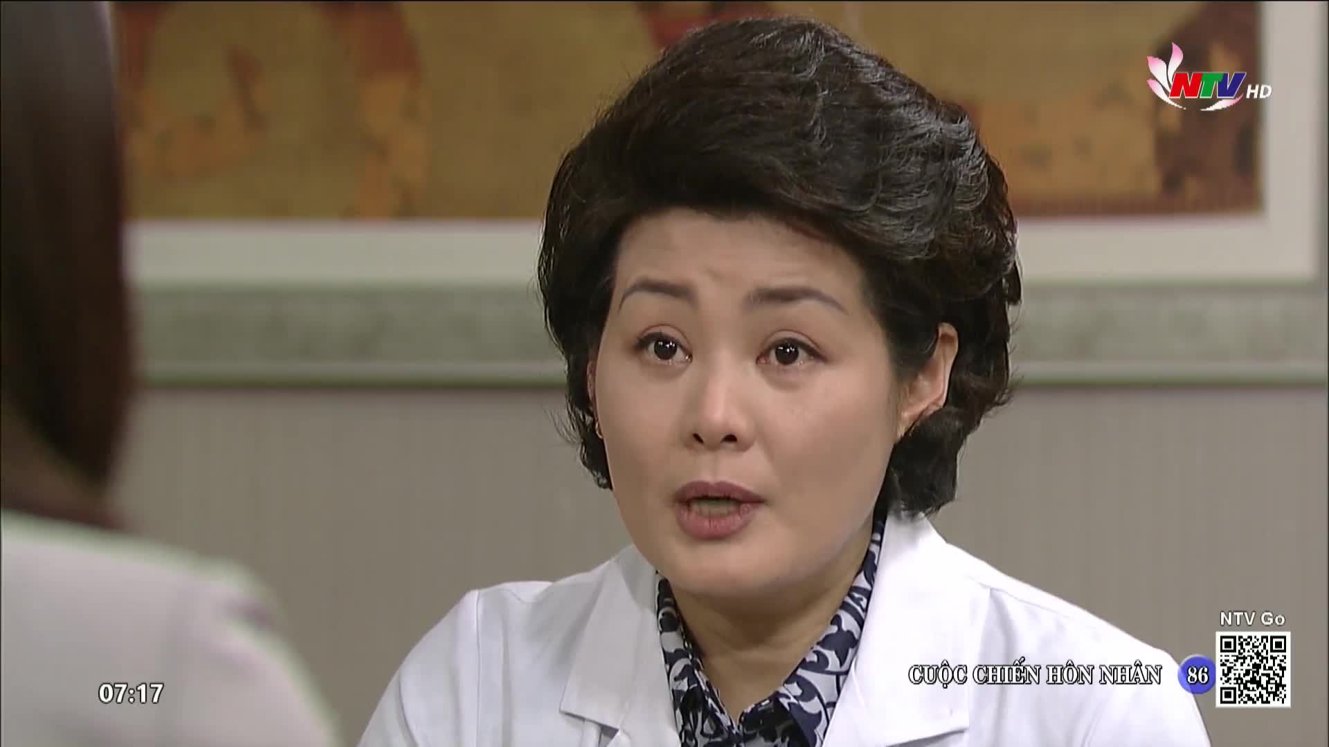 A woman in a white coat, likely a doctor, is speaking, her mouth open as if mid-sentence. The Nghe An TV logo is visible in the corner, and the show's title, "Cuộc Chiến Hôn Nhân," appears below.
