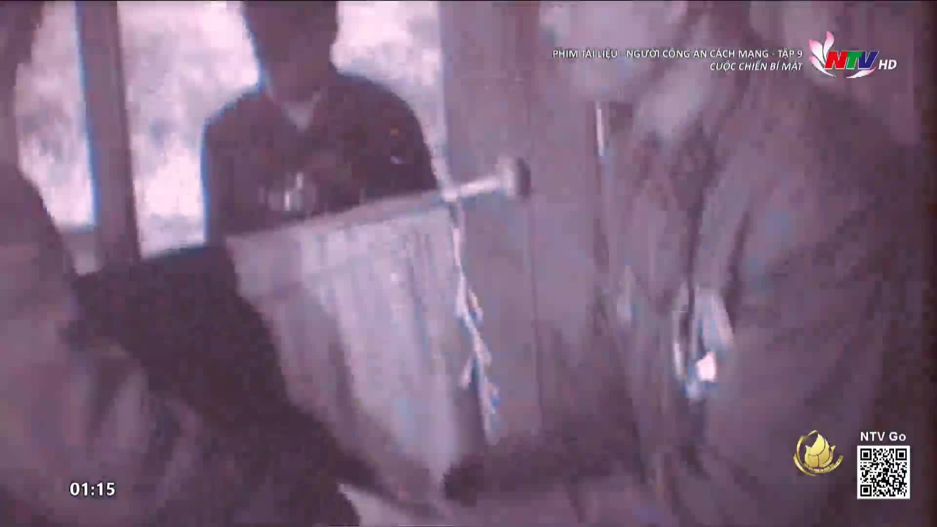 A man swings a long, thin object, possibly a baton, towards another person. The scene is dim, and the grainy quality suggests it's a recording from a Vietnamese television program.
