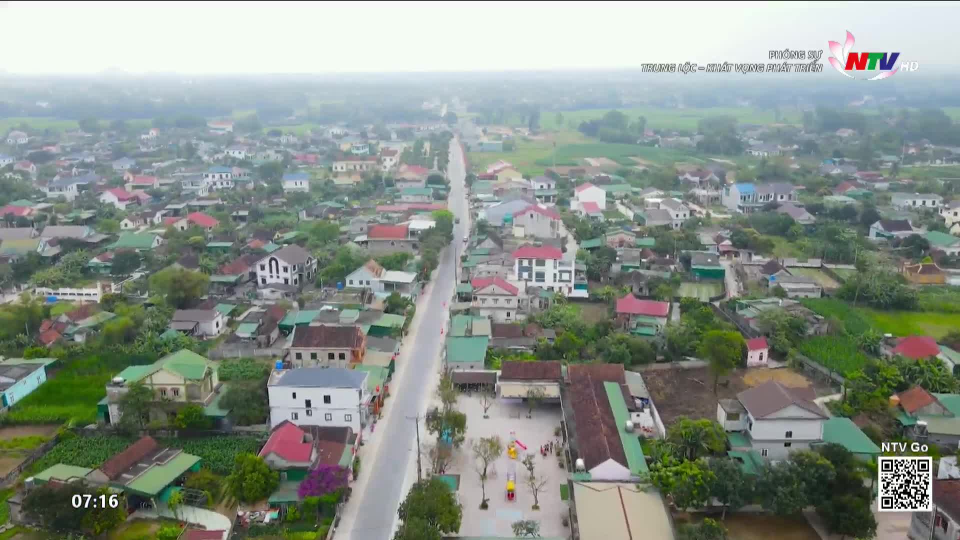 From the elevated perspective, a long road cuts through a Vietnamese village, lined with houses of varying sizes and colors. The Nghe An TV logo is visible in the corner, and the scene is bathed in a soft, overcast light.
