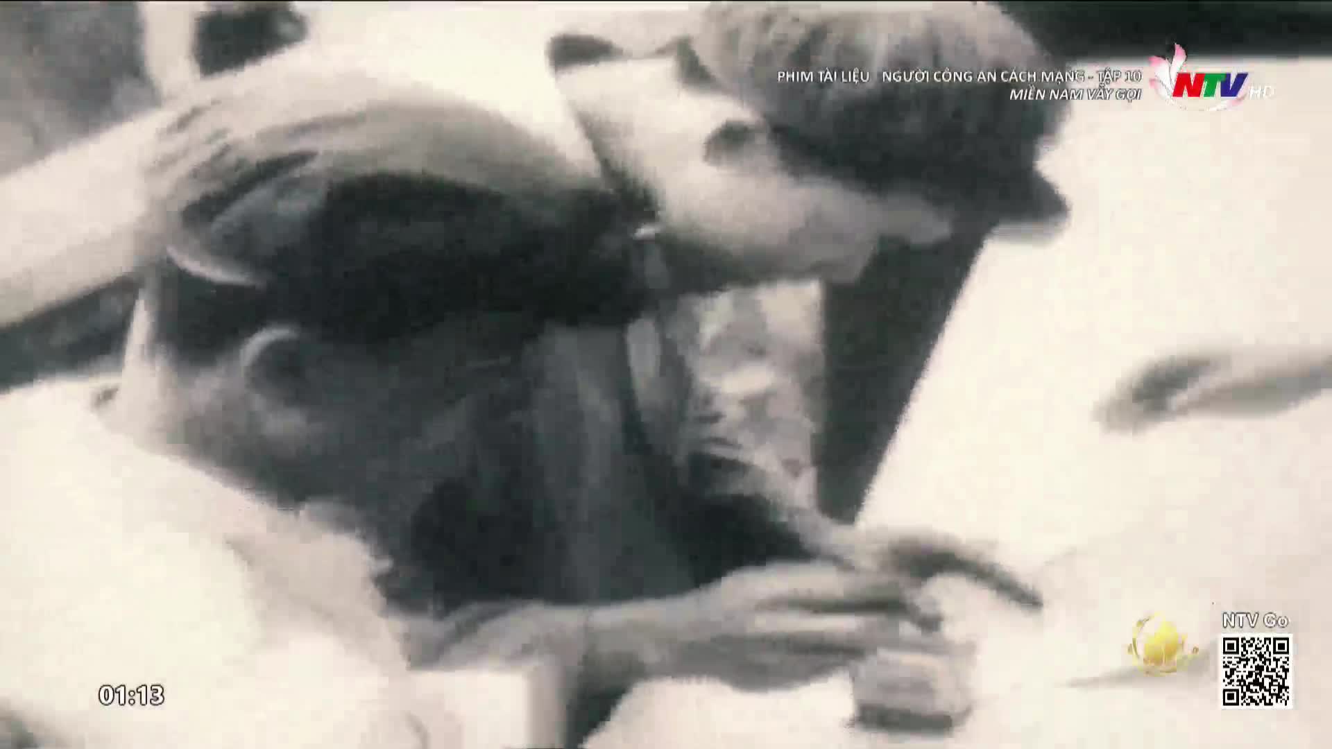 A man leans over, his face close to the surface of a table, possibly examining something. The scene appears to be from a documentary on Nghe An TV, as indicated by the logo.

