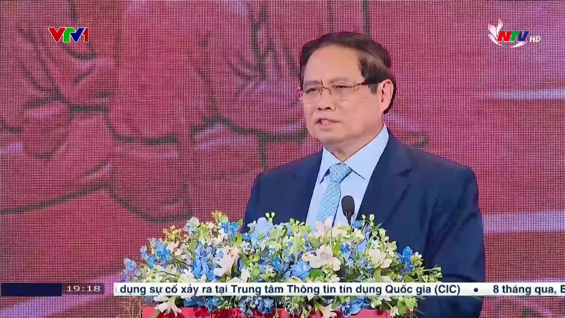 A man in a suit, speaking into a microphone, stands behind a podium adorned with flowers. The scene is being broadcast on Nghe An TV, with the VTV1 logo in the corner.
