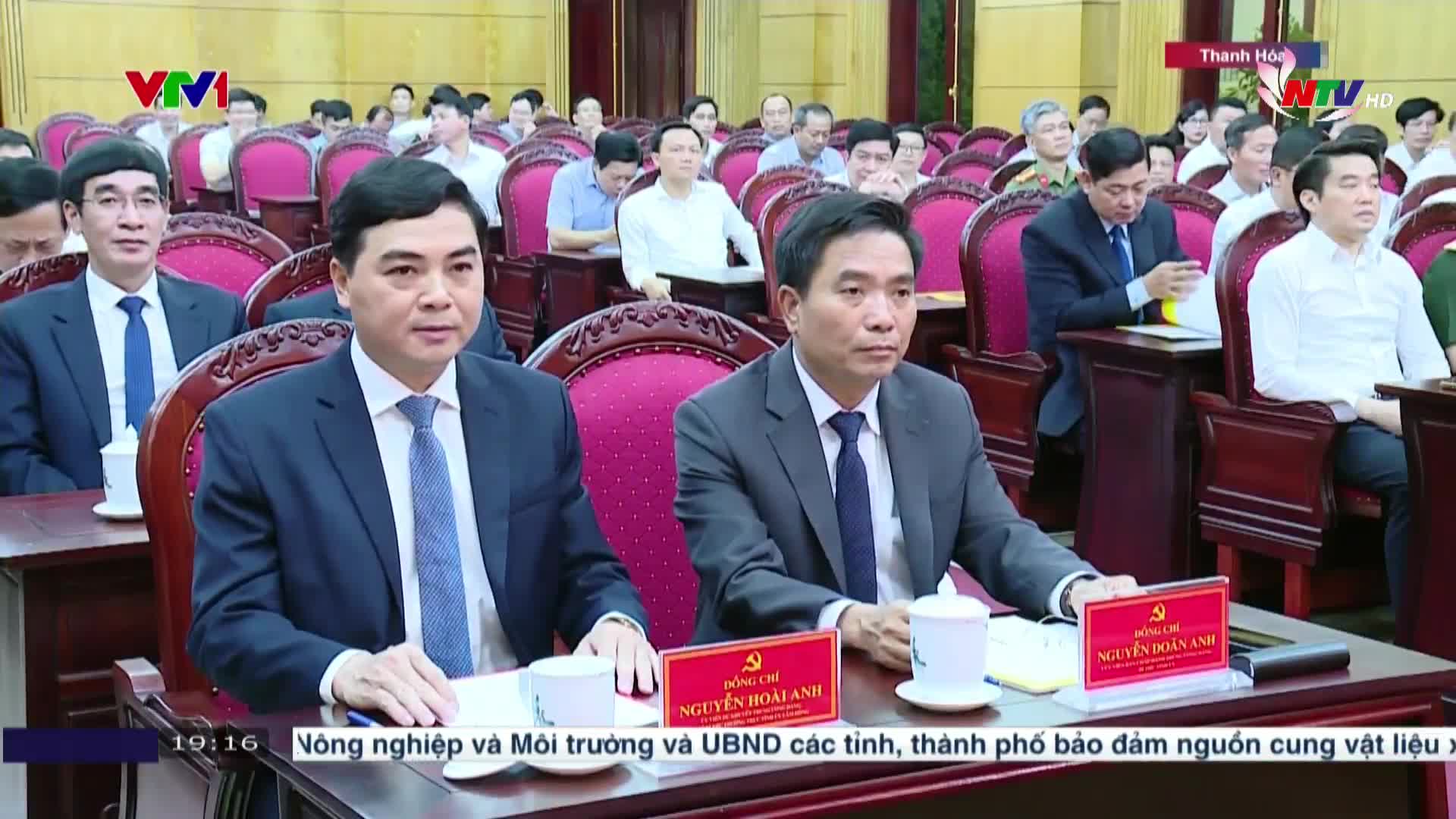 Men in suits sit at a long table, facing the camera, with a crowd of people behind them. The scene is being broadcast on Nghe An TV, with a VTV logo in the corner.
