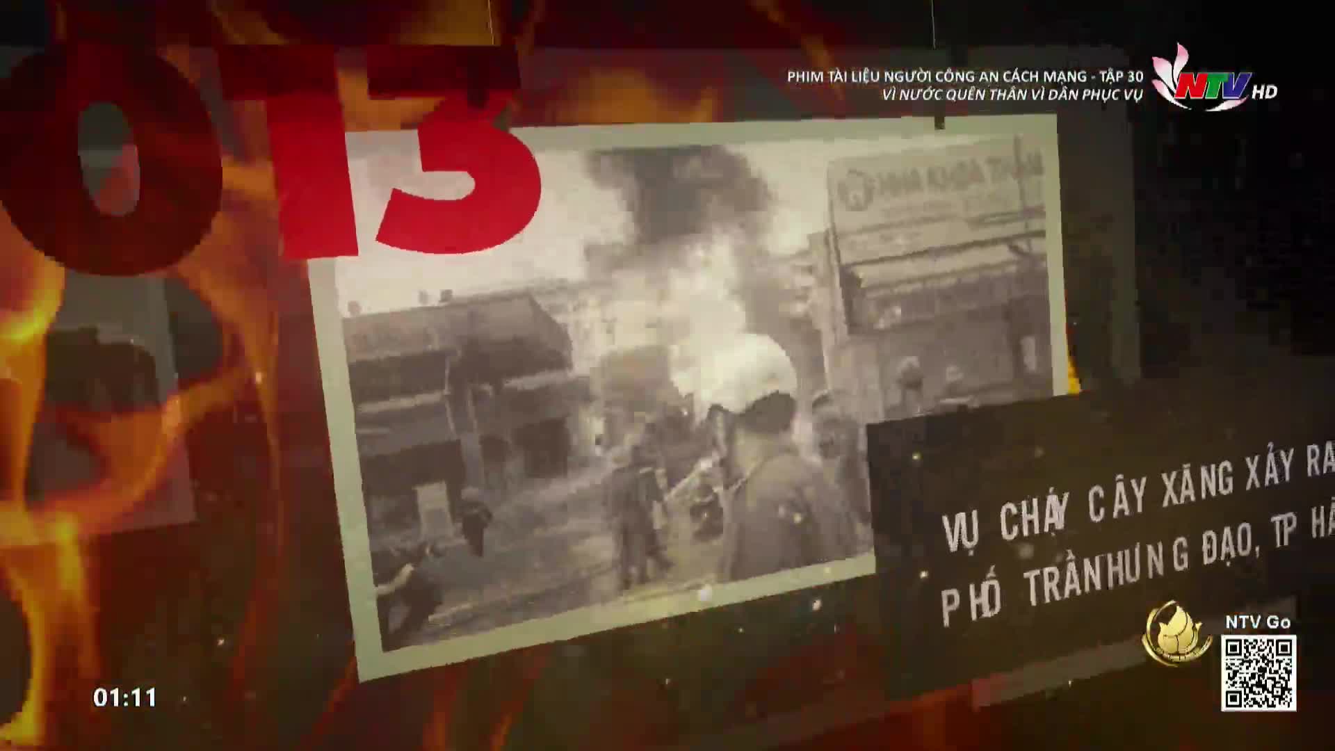 The screen shows a black-and-white image of a fire, with people in uniform standing in front of it. A large red "13" and flames overlay the scene, part of a program on Nghe An TV.
