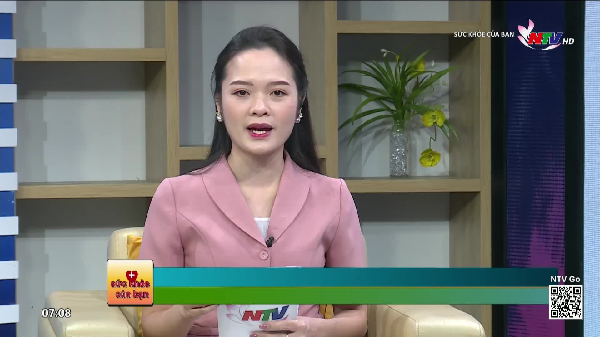 A woman in a pink blazer speaks directly to the camera, seated in a studio setting. The Nghe An TV logo and the words "Suc Khoe Cua Ban" are visible on the screen.

