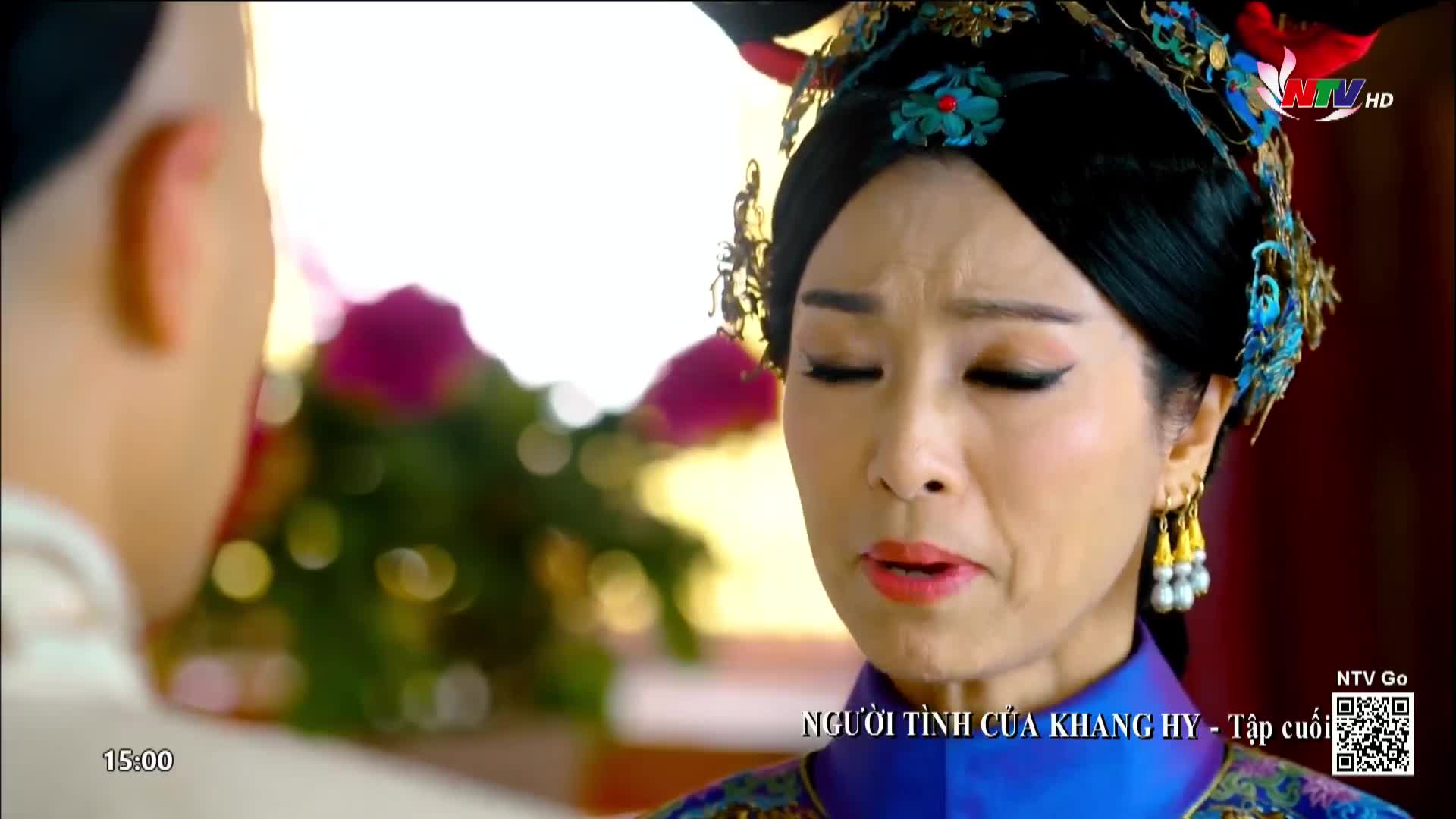 A woman with elaborate headwear and makeup cries, her eyes closed. The scene, broadcast on NTV Go, appears to be from a Vietnamese drama.