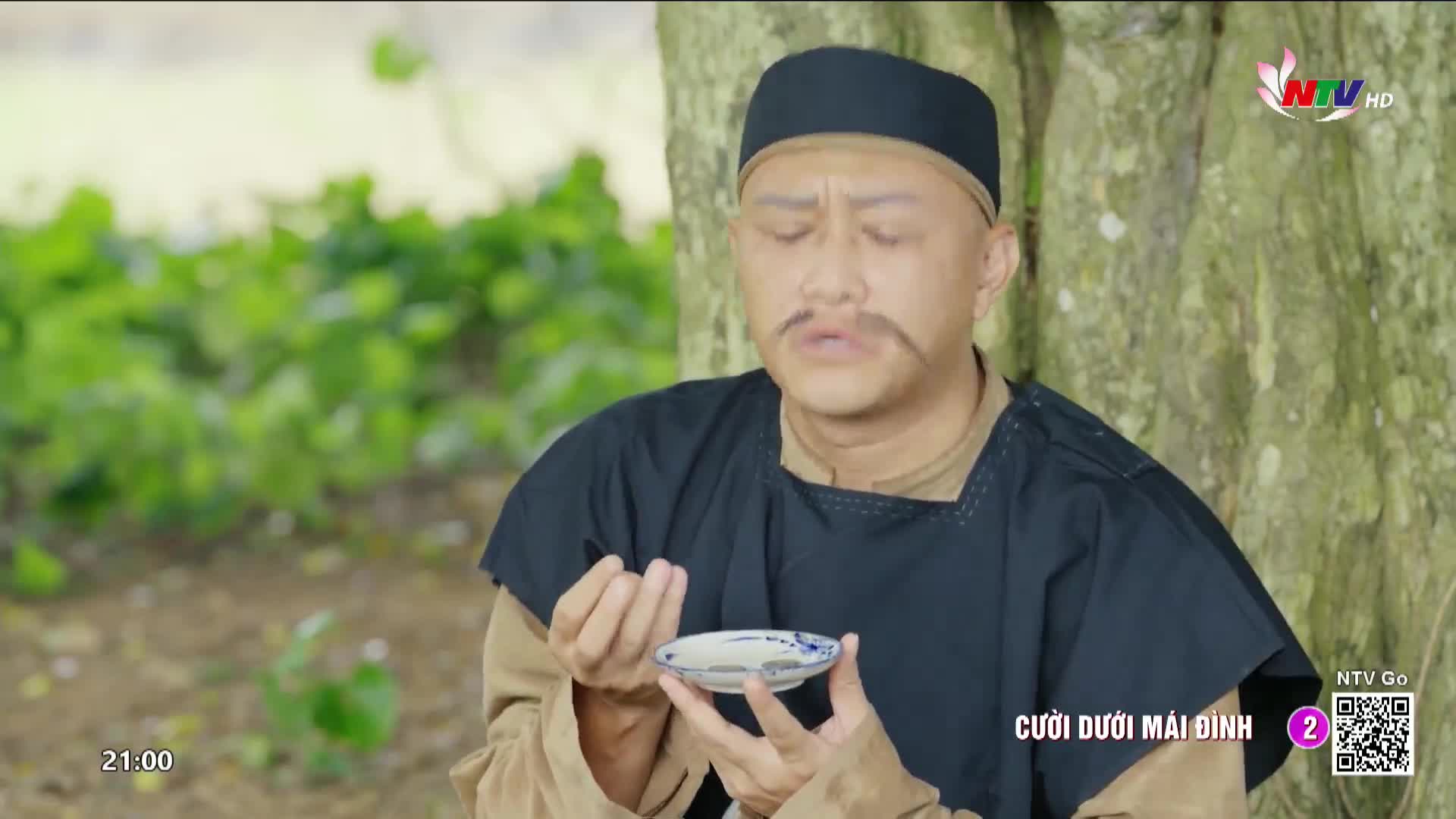 A man in traditional Vietnamese attire holds a small, patterned dish, his expression thoughtful. The Nghe An TV logo is visible in the corner, suggesting this is a scene from a broadcast.