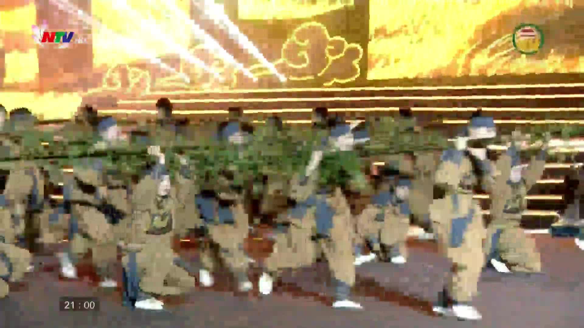 A group of performers in traditional Vietnamese attire moves in unison, holding long bamboo poles. The NTV broadcast captures this vibrant display against a backdrop of bright, illuminated patterns.