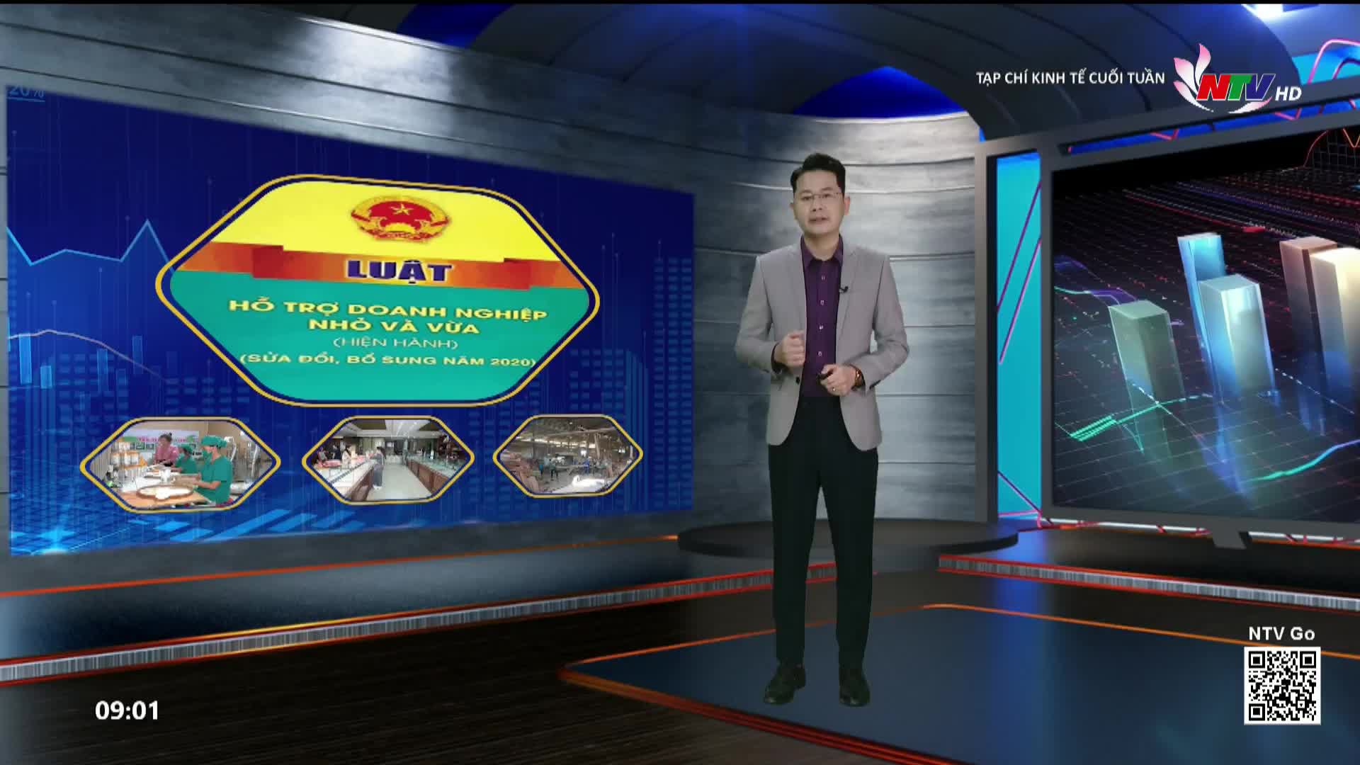 A man in a light gray suit stands in a studio, facing a large screen displaying Vietnamese text and images of businesses. To his right, another screen shows a 3D bar graph with a blue and green grid overlay.