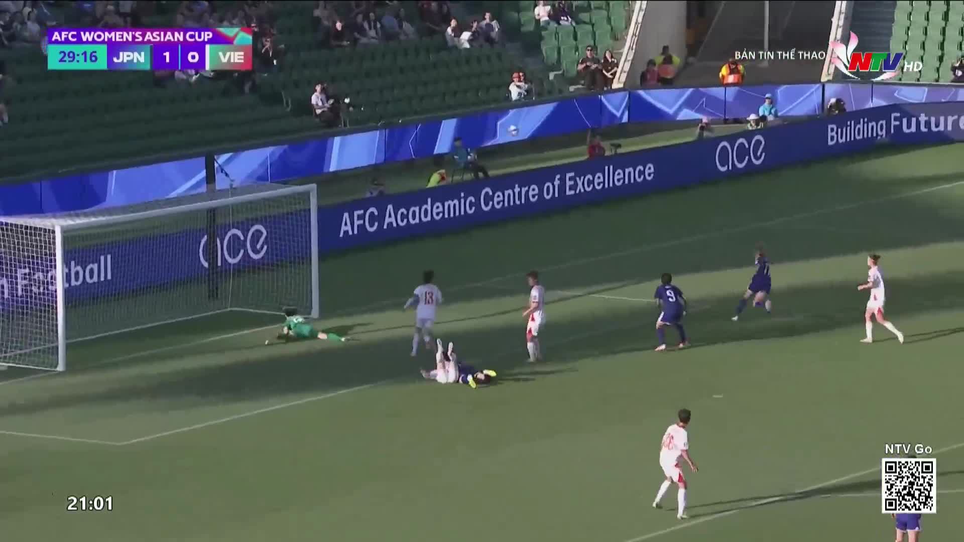 A Vietnamese player goes down near the goal as a Japanese player in white and blue slides to make a play. The scoreboard shows Japan leading Vietnam 1-0.