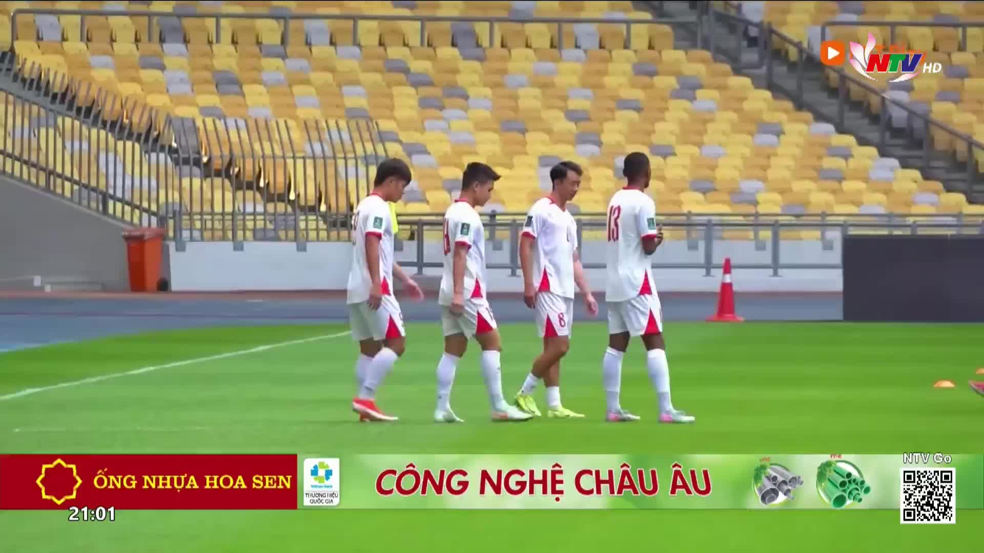 Four young men in white soccer kits walk across the green pitch, their red trim bright against the grass. The stands behind them are filled with yellow seats, a familiar sight at a stadium in Nghe An.