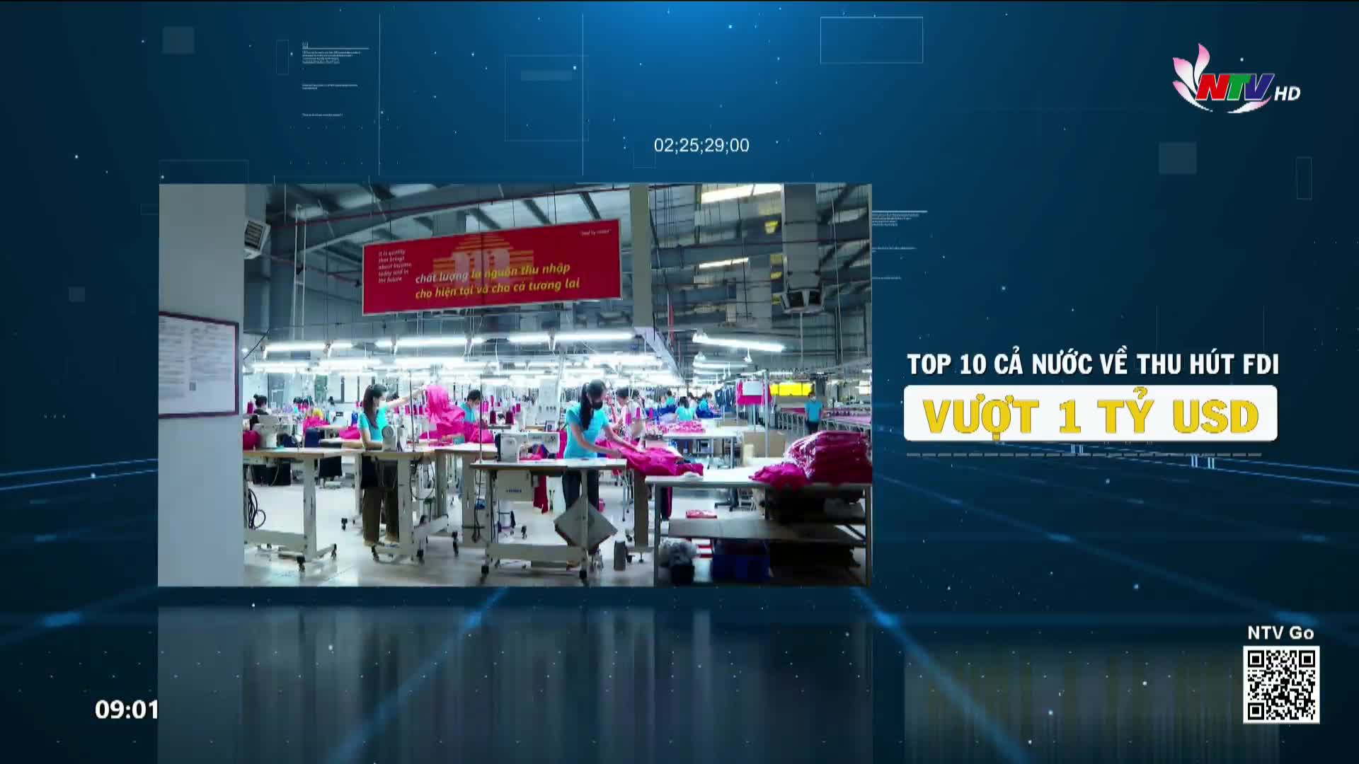 Workers in bright pink shirts stand at sewing machines in a large factory. A red banner hangs above them, displaying Vietnamese text.