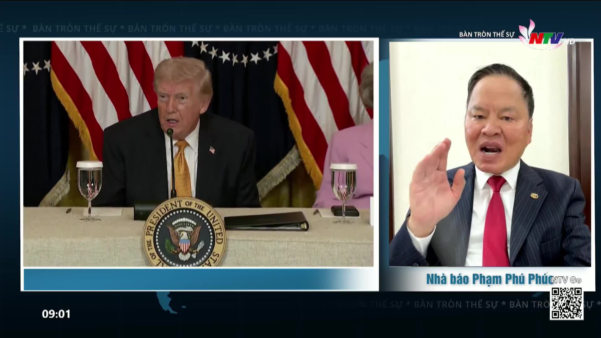 A man in a dark suit and red tie gestures with his right hand as he speaks on a screen, while another man in a dark suit and yellow tie sits behind a table with an American flag in the background. The Nghe An TV logo appears in the corner of the screen.