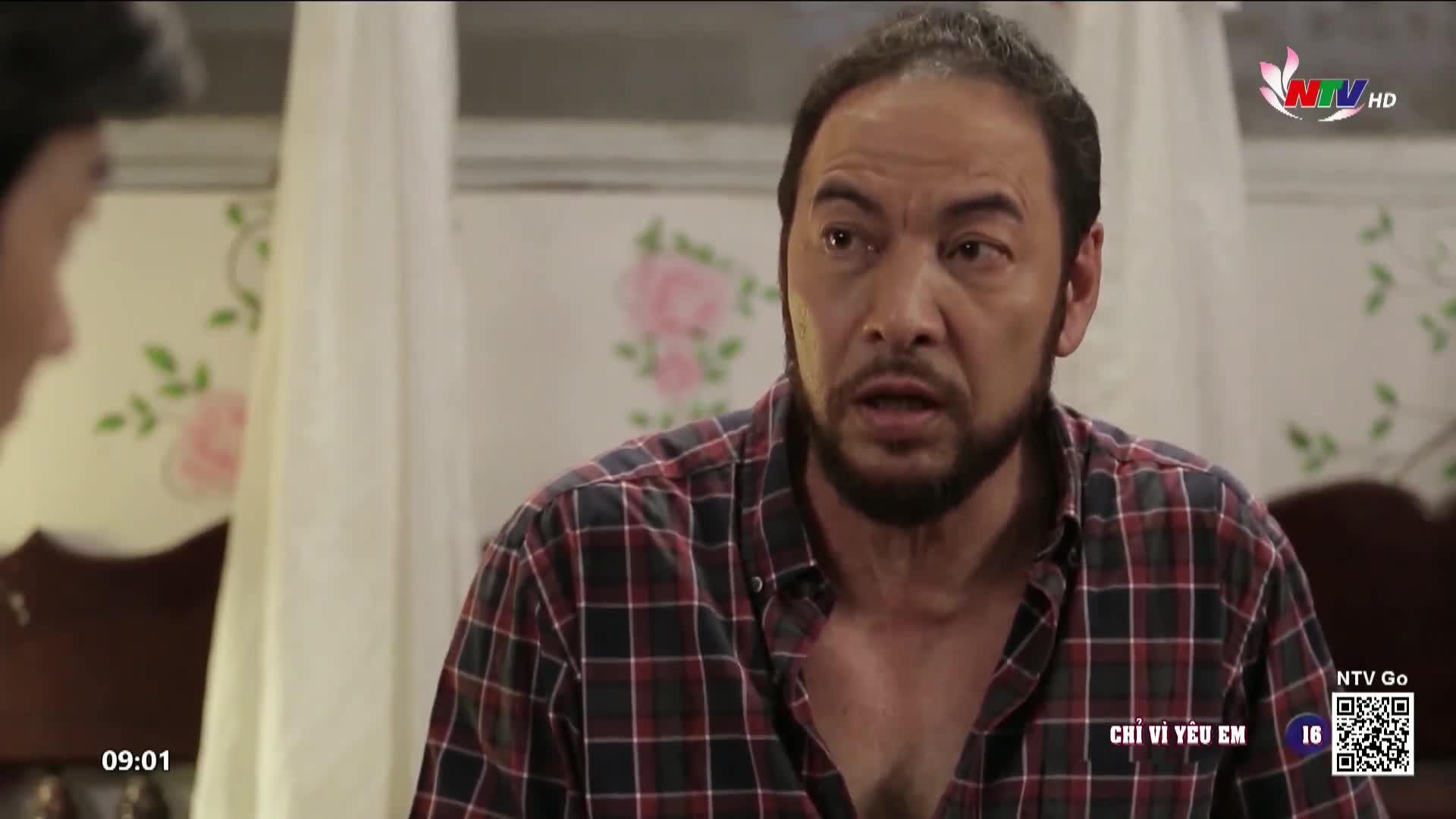 A man with a beard and a plaid shirt speaks intensely, his brow furrowed. The scene is from a Vietnamese drama, likely broadcast on Nghe An TV.