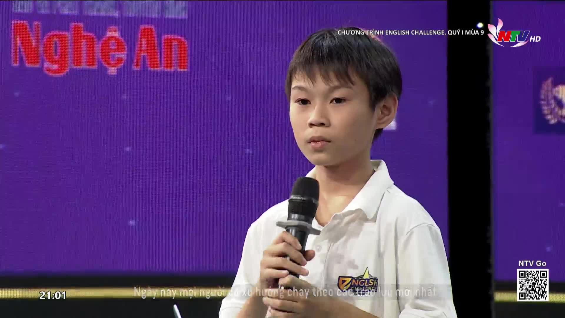 A young boy stands on a stage, holding a microphone. The backdrop behind him displays "Nghe An" in large red letters, indicating this is a broadcast from Vietnam.