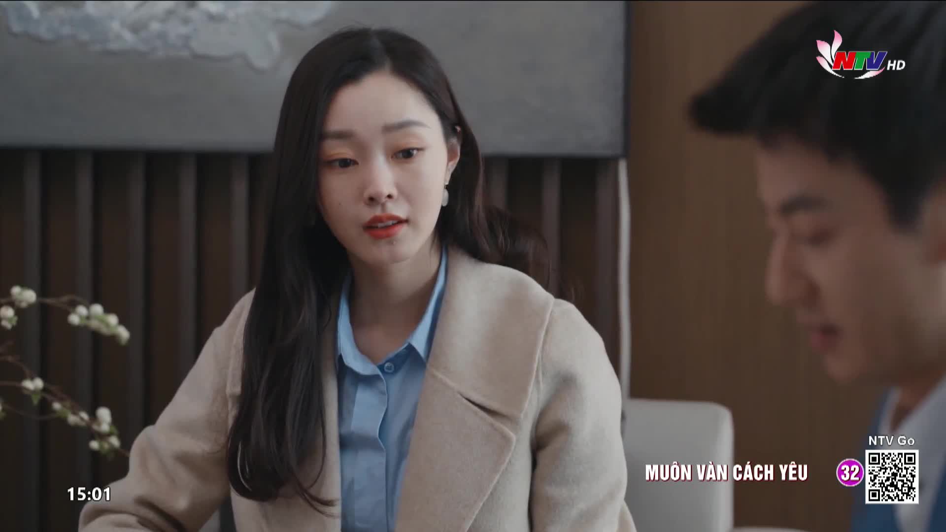 A young woman with long, dark hair and a light blue shirt under a beige coat speaks, her expression earnest. Beside her, a young man looks down, his face partially obscured. The Nghe An TV logo appears in the upper right corner.