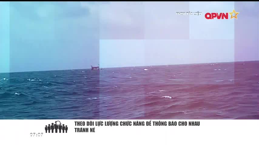 The sea is choppy, with small whitecaps breaking across the surface. A structure, possibly a platform or a vessel, sits in the distance under a cloudy sky, seemingly part of a QPVN broadcast.
