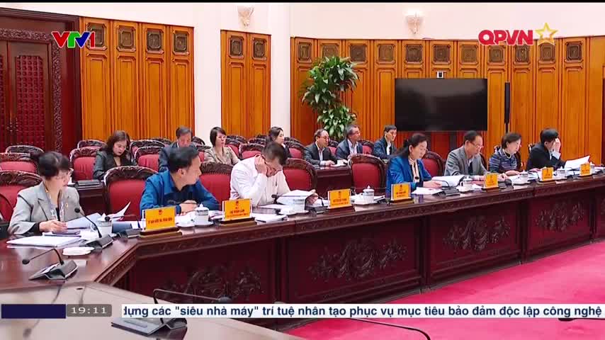 A meeting is underway, with a long table of officials in a wood-paneled room. Papers and nameplates are spread out before them as they listen to a presentation, likely broadcast on QPVN.
A meeting is underway, with a long table of officials in a wood-paneled room. Papers and nameplates are spread out before them as they listen to a presentation, likely broadcast on QPVN.