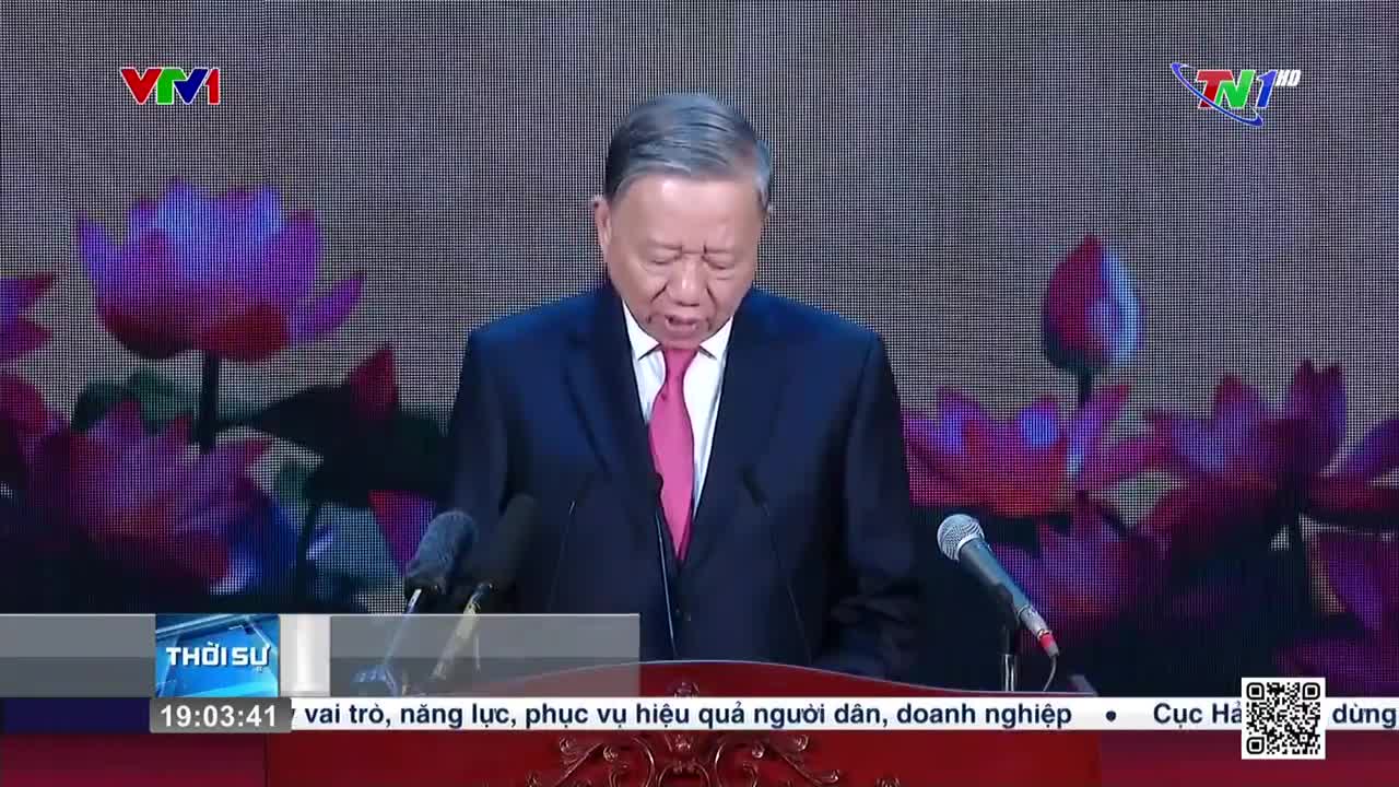 A man in a suit, speaking into a microphone, stands before a backdrop of lotus blossoms. The broadcast is on Thai Nguyen TV, with the VTV1 logo visible in the corner.
