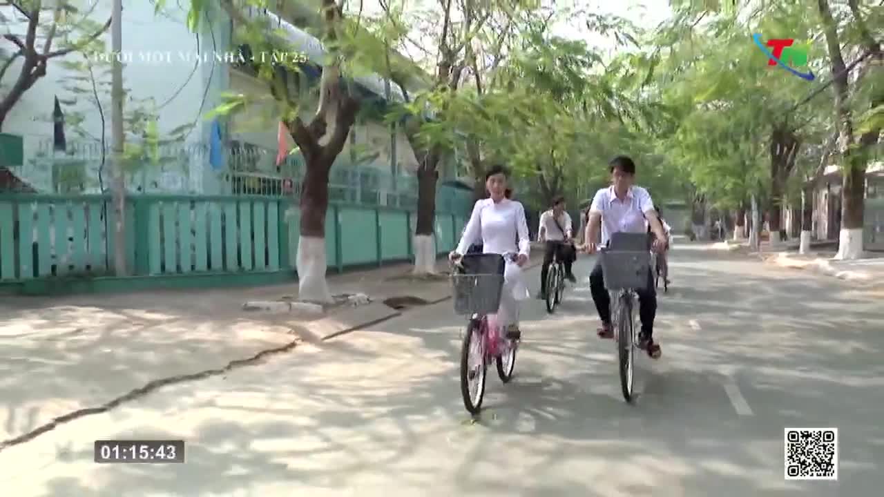 A group of people in white shirts and black pants pedal bicycles down a tree-lined street. The scene is part of a broadcast from Thai Nguyen TV in Vietnam, with a time stamp at the bottom left.
