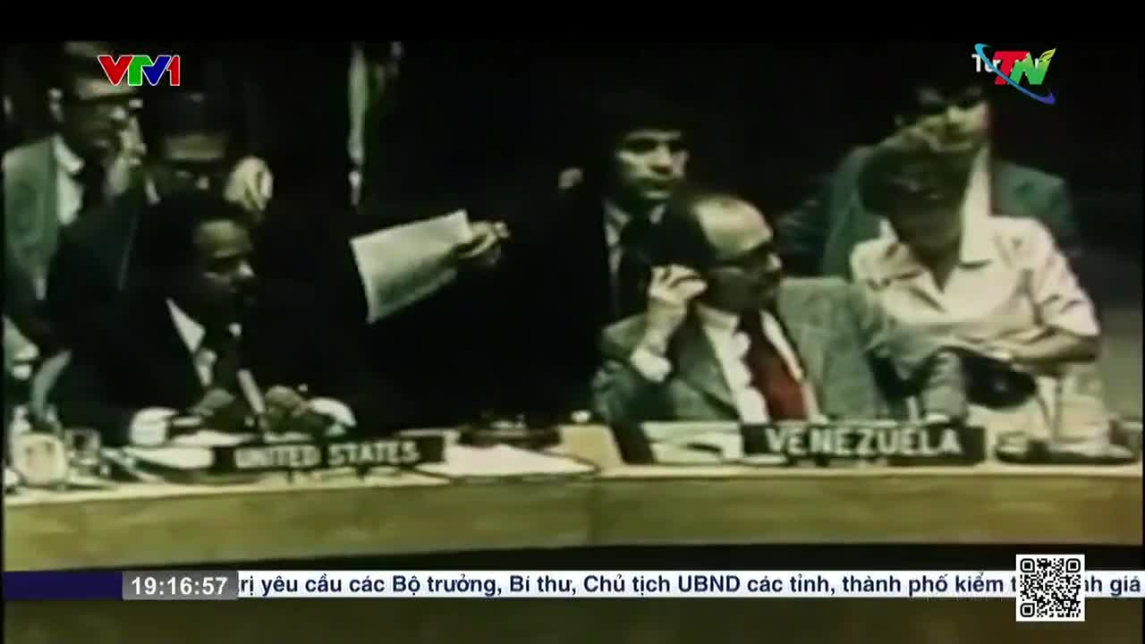 Men in suits sit at a long table, some with papers, others on the phone. The "United States" and "Venezuela" signs in front of them indicate the setting, likely a conference, as broadcast by Vietnam Television.
