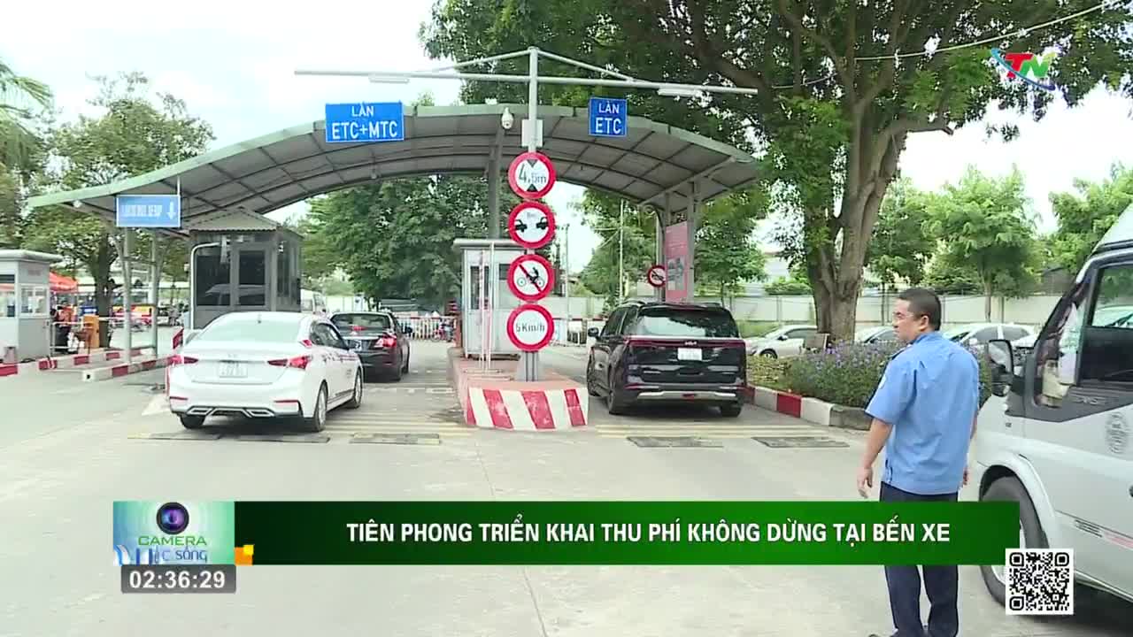 Cars are slowly passing through a toll booth, under a metal canopy marked "ETC+MTC" and "ETC". A man in a blue shirt stands near a white van, watching the vehicles.
