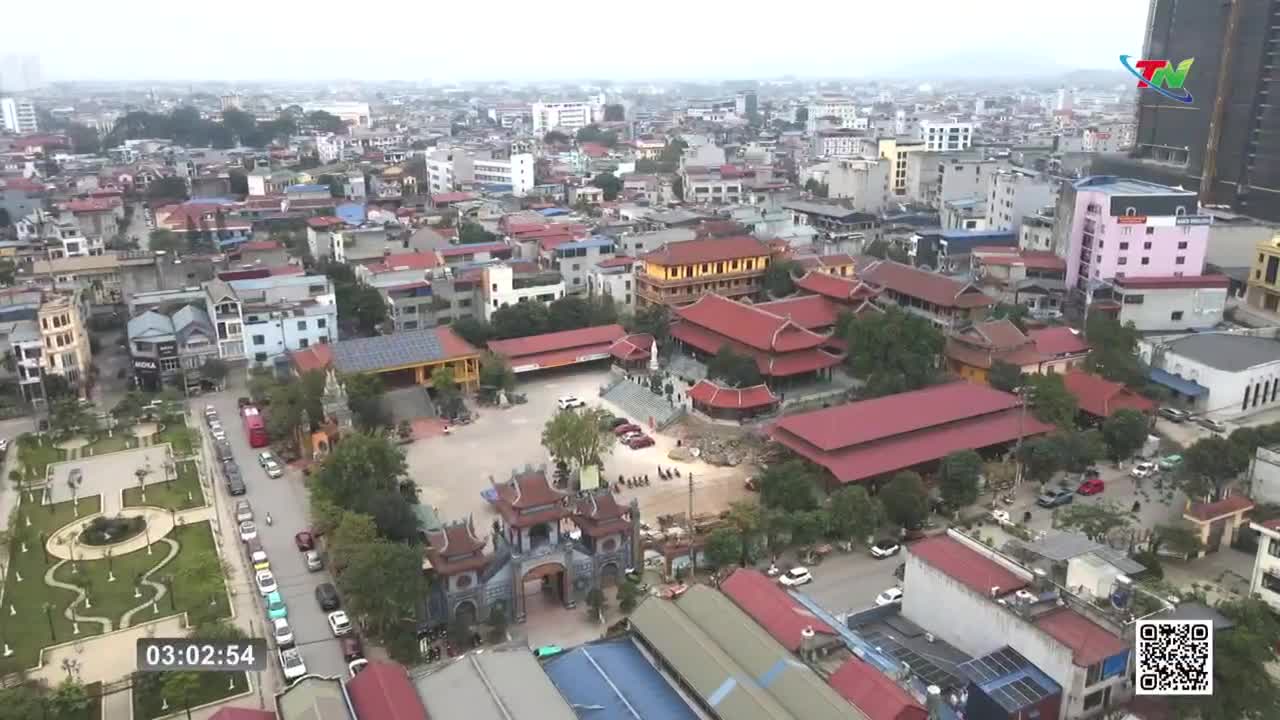 Cars are parked along a street next to a park and a temple complex. The red-tiled roofs of the temple stand out against the urban sprawl of Thai Nguyen.