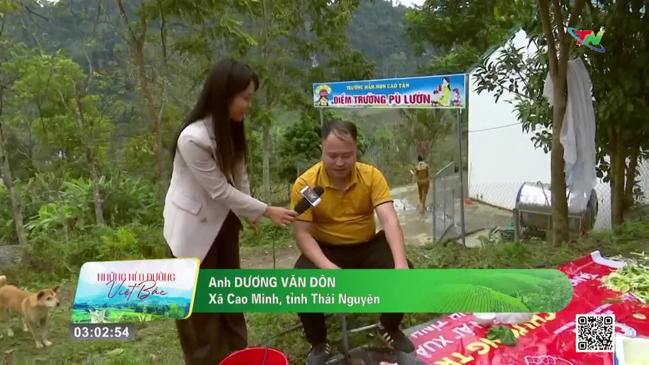 A reporter holds a microphone to a man sitting on a stool. Behind them, a sign for a kindergarten hangs above a doorway.