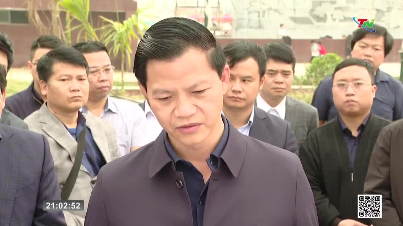 A man in a dark jacket speaks, his expression serious. Behind him, a group of men stand attentively, some in suits, others in more casual attire, as if at an official gathering in Thai Nguyen.