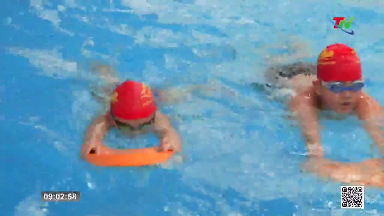 Two young swimmers, wearing red caps, glide through the blue water. One holds an orange kickboard, propelling themselves forward with steady strokes. Two young swimmers, wearing red caps, glide through the blue water. One holds an orange kickboard, propelling themselves forward with steady strokes.