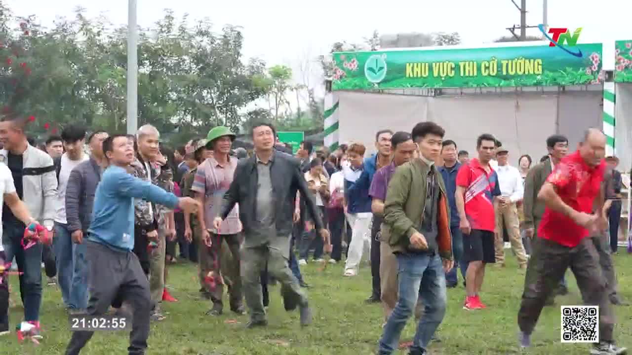 A man in a blue shirt winds up to throw something, his face contorted in concentration. Behind him, a crowd watches the event unfold, a banner in Vietnamese overhead.