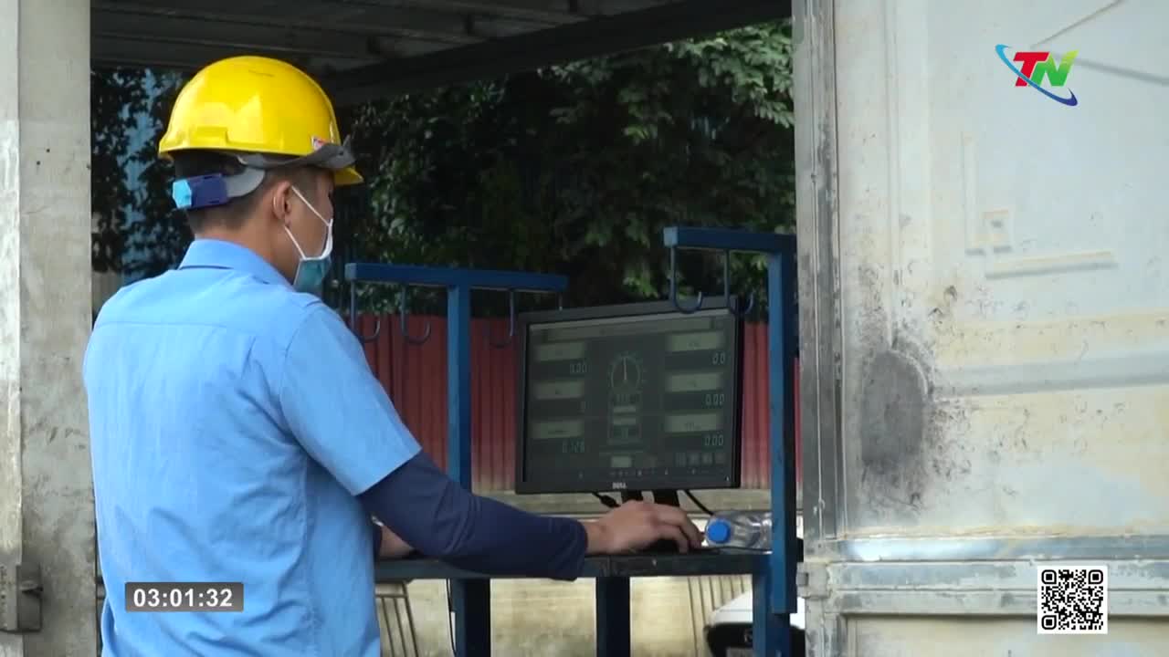 A worker in a blue shirt and yellow hard hat stands at a control panel, his hand on a dial. The screen displays numbers and a dial graphic, likely part of operations in Thai Nguyen.