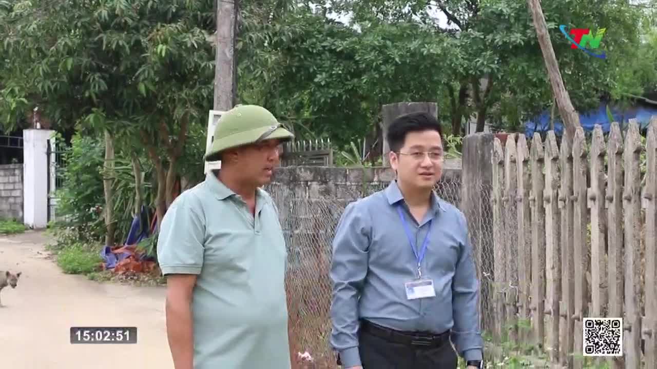 Two men stand on a dirt path, one in a green helmet and polo shirt, the other in a blue button-down. A small dog trots past them on the left. Two men stand on a dirt path, one in a green helmet and polo shirt, the other in a blue button-down. A small dog trots past them on the left.