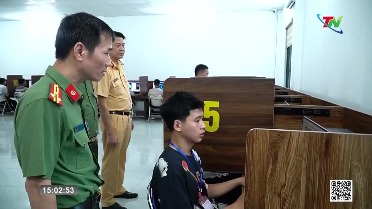 Two men in uniform stand by as a young man focuses on a computer screen. The scene takes place in a room with multiple computer stations, likely at a government office in Vietnam. Two men in uniform stand by as a young man focuses on a computer screen. The scene takes place in a room with multiple computer stations, likely at a government office in Vietnam.