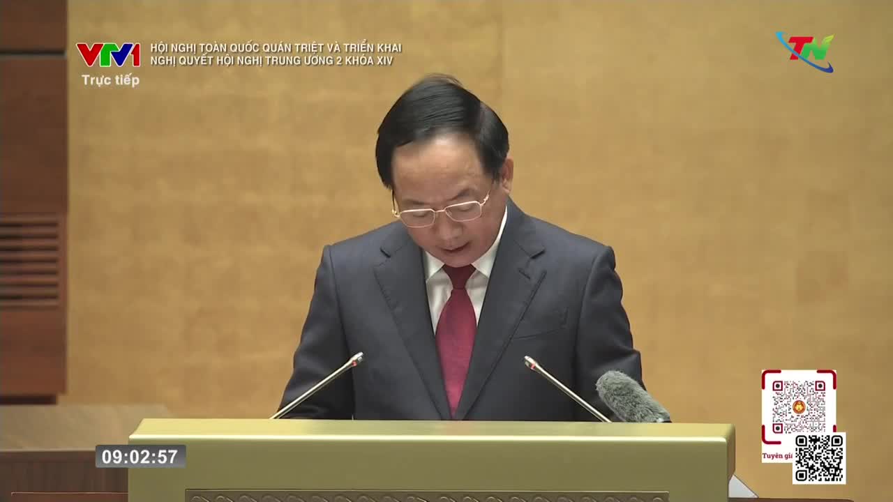 A man in a dark suit and red tie stands at a podium, reading from a paper. The broadcast, live from Vietnam, shows the VTV logo in the corner. A man in a dark suit and red tie stands at a podium, reading from a paper. The broadcast, live from Vietnam, shows the VTV logo in the corner.