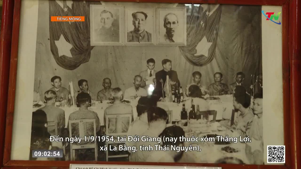 A group of men are seated at tables, some standing to speak. Portraits hang above them, and flags drape the wall behind. The scene is from a gathering in Thai Nguyen province. A group of men are seated at tables, some standing to speak. Portraits hang above them, and flags drape the wall behind. The scene is from a gathering in Thai Nguyen province.