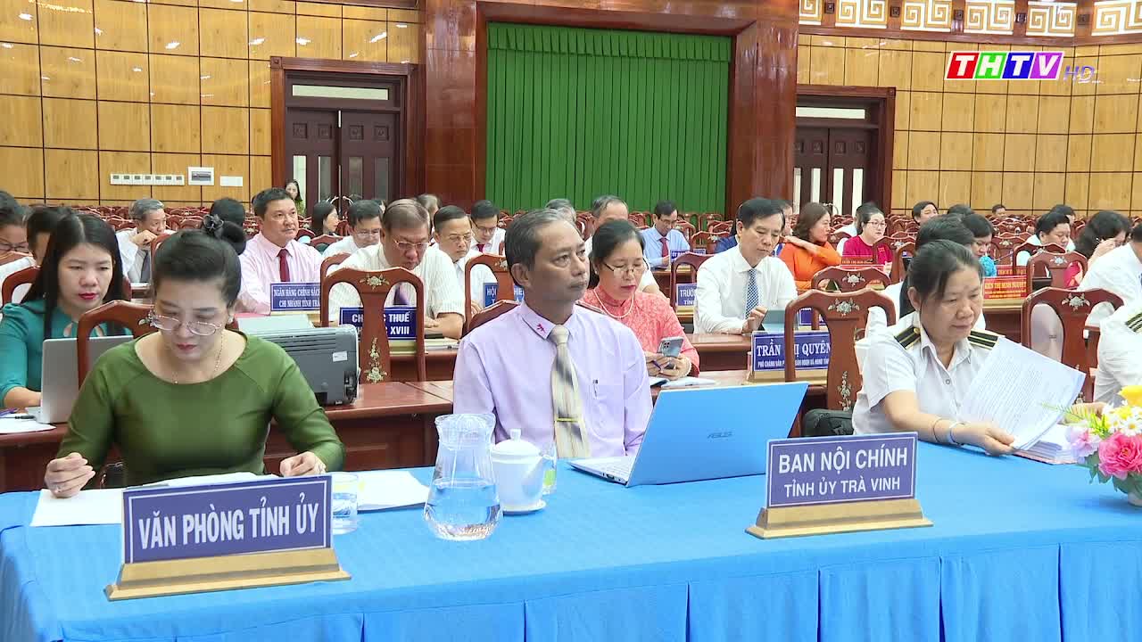 In a large room, officials are seated at tables, papers and laptops in front of them. The Tra Vinh TV logo is visible in the corner of the screen, and a meeting is underway.
