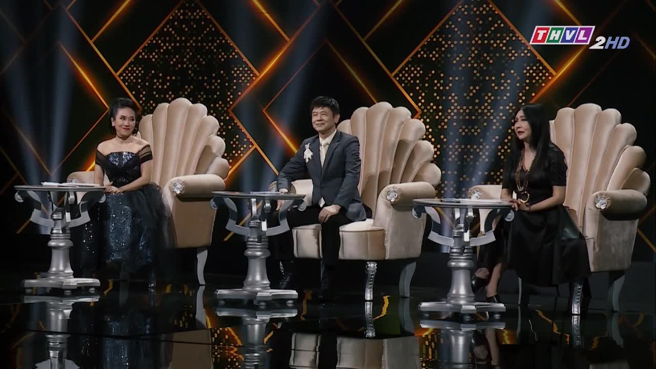 Three people sit on ornate chairs, each with a small table in front of them. The stage is lit with a dramatic backdrop, likely for a show on Tra Vinh TV in Vietnam.

