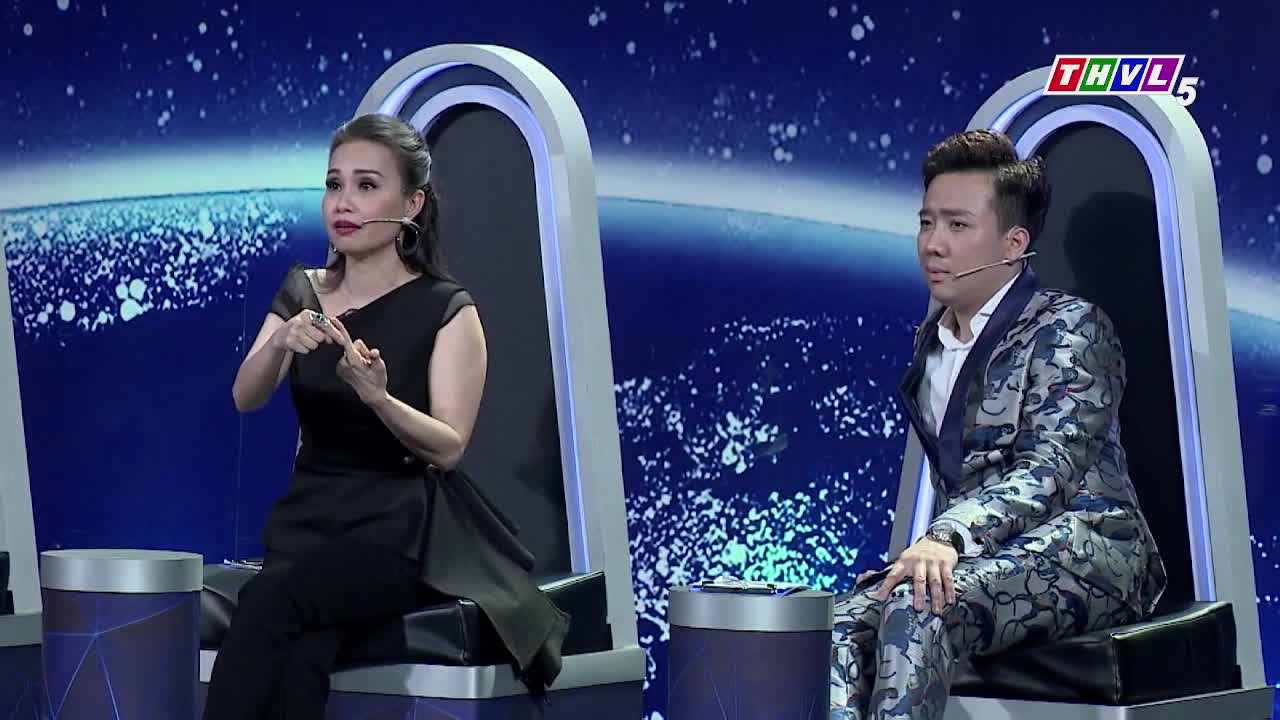 A woman in black gestures with her hands, while a man in a patterned suit sits beside her, looking toward the side. The background is a blue screen, and the logo for THVL5 is visible.
