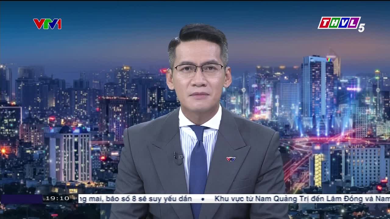 A man in a suit and glasses is speaking, framed against a cityscape backdrop, the THVL5 logo visible in the corner. Below, a news ticker scrolls with Vietnamese text.
