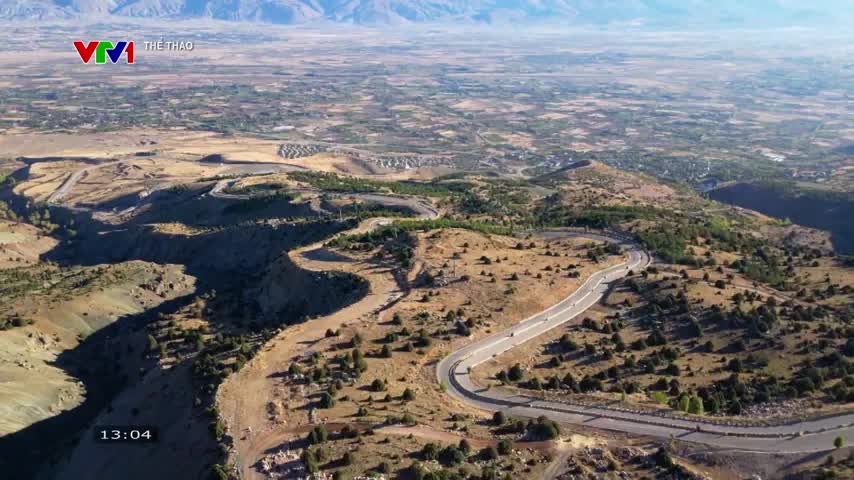 A winding road snakes through a dry, hilly landscape, and a few tiny vehicles are visible. The broadcast is on VTV1, and the time is just after 13:00.
