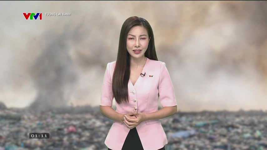 A woman in a pink blazer stands before a backdrop of a smoldering landfill, speaking on VTV1 in Vietnam. Thick smoke billows from the waste, filling the air behind her.
