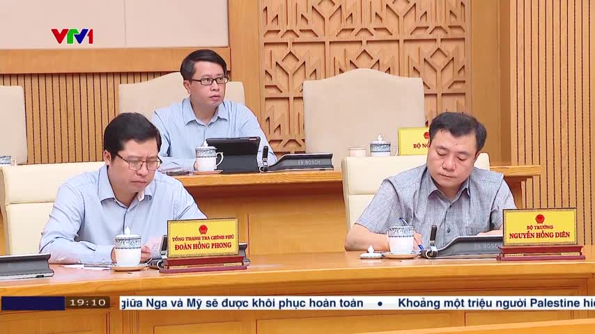 Three men in shirts sit at a long wooden table, each with a nameplate in front of them. The VTV1 logo is visible in the upper left corner, and the time is 19:10.
