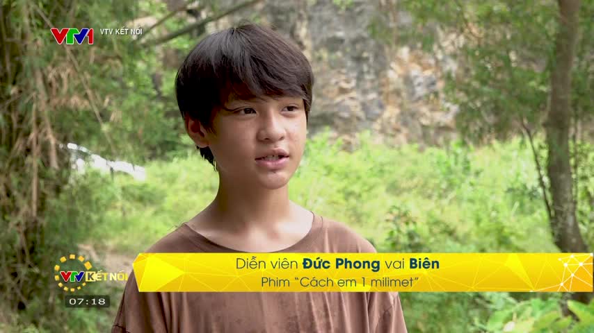 A young man stands in front of a lush, green backdrop, speaking into the camera. A yellow banner at the bottom identifies him as Đức Phong, the actor playing Biên in the film "Cách em 1 milimet," which is airing on VTV1.
