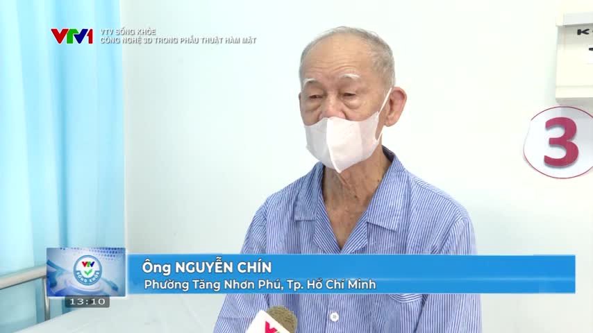 An elderly man in a mask and hospital gown speaks into a microphone, likely for a VTV1 segment. The scene takes place in what appears to be a hospital room in Vietnam, with a large "3" on the wall.
