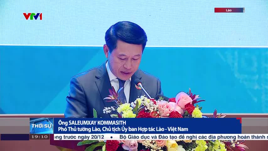 On VTV1, a man in a dark suit speaks into a microphone, his words likely broadcast across Vietnam. Beneath him, a lower third identifies him as a Lao official, with the news ticker running below.
