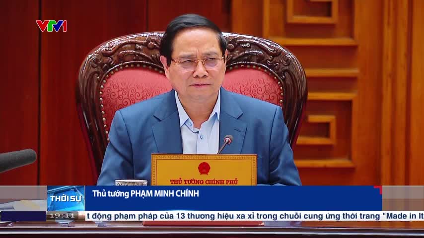 Pham Minh Chinh, the Prime Minister, sits at a table, facing the camera. The VTV1 news ticker below displays the time and a headline about luxury brands.
