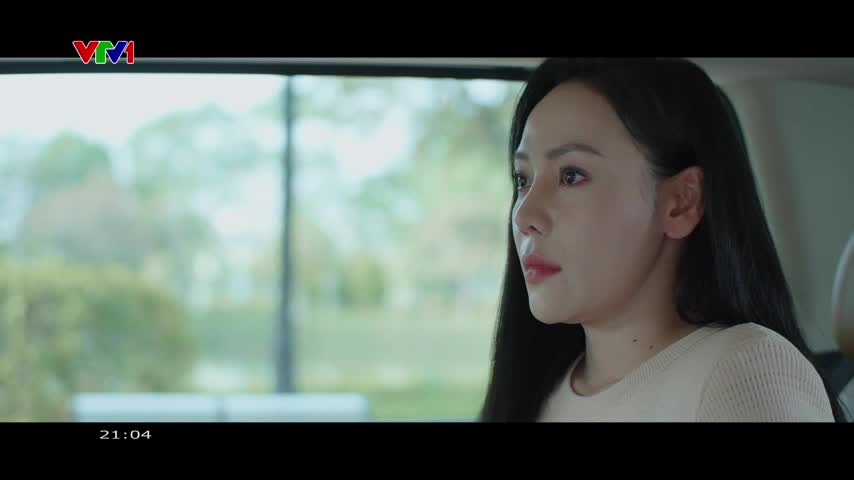 The car moves through a green landscape, trees and bushes blurring past the window. A woman with dark hair gazes out, her expression thoughtful.
