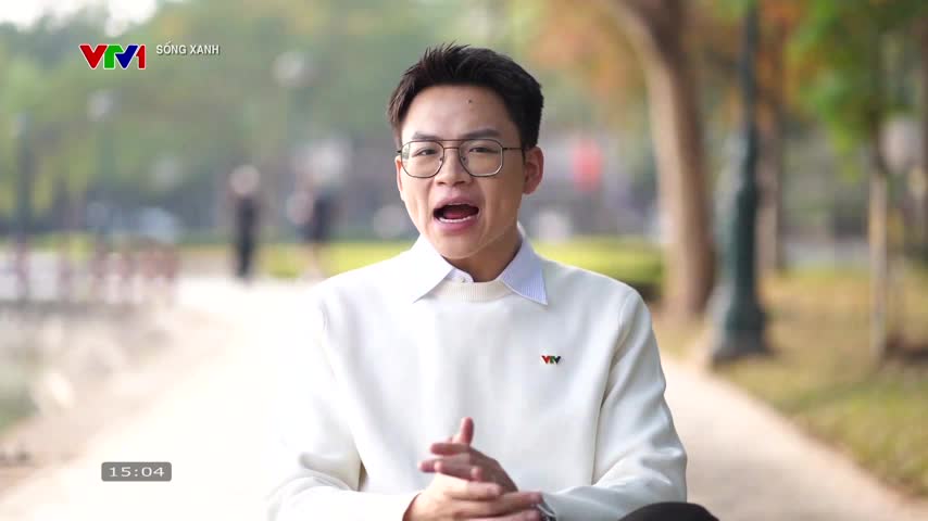 A young man in a white sweater speaks animatedly outdoors, the VTV1 logo visible on his chest. The background shows a blurred park scene with trees and a path.